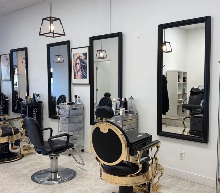 Modern hair salon interior featuring gold and black barber chairs, large wall mirrors, and glass display shelves.
