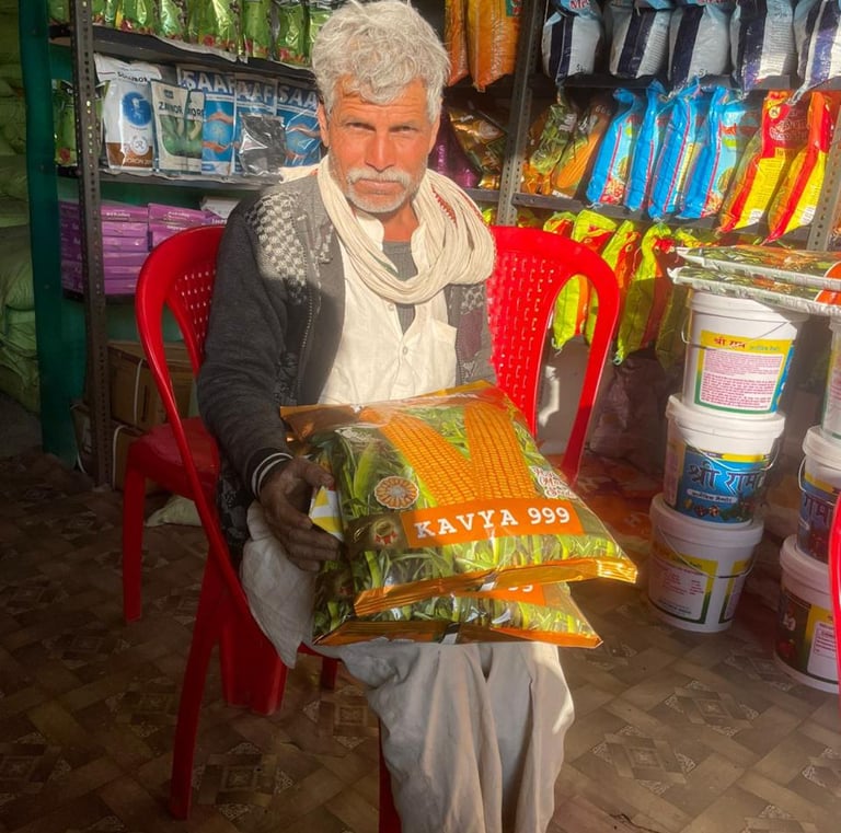 Indian farmer sitting in a supply store holding bags of Kavya 999 hybrid corn seeds.