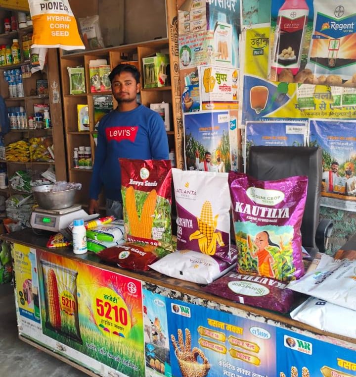 Shopkeeper at an Indian agriculture store with hybrid corn and vegetable seeds for farming.