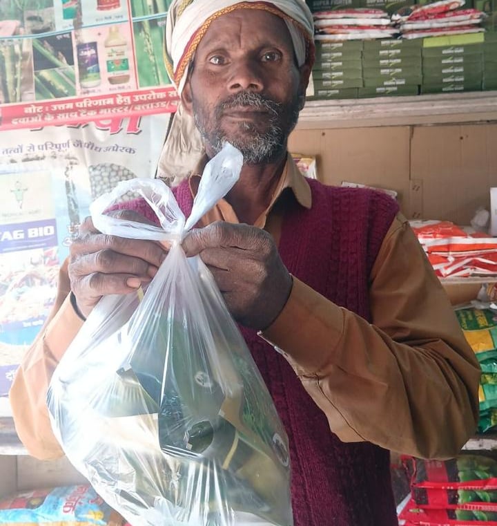 An Indian farmer holding a plastic bag of seeds inside an agricultural supply store.