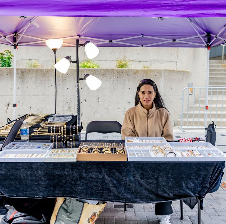 A female artisan selling handmade jewelry at an outdoor Afro Fiesta Festival vendor booth.
