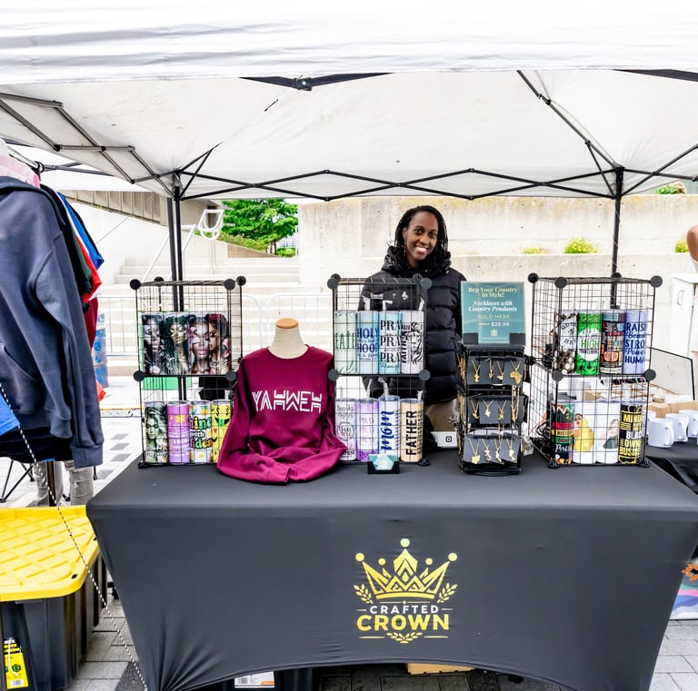 A smiling vendor showcases custom apparel and printed tumblers at the Crafted Crown booth during the Afro Fiesta Festival.