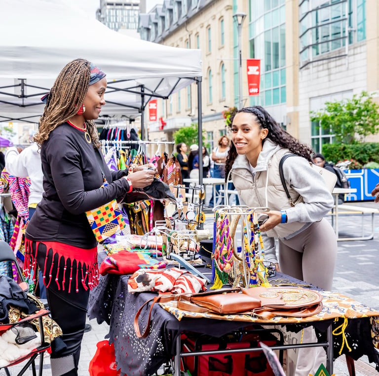 A customer shops for handmade African jewelry and accessories at an outdoor Afro Fiesta Festival market stall.