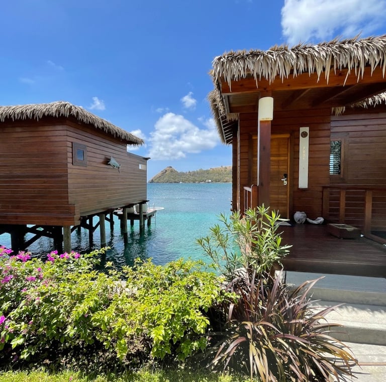 Luxury overwater wooden bungalows with thatched roofs overlooking tropical turquoise ocean water.