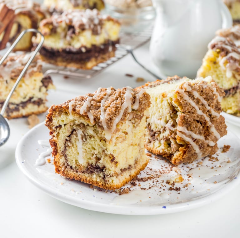 Slices of moist coffee cake with a cinnamon swirl and crumble topping, drizzled with white glaze on a plate.