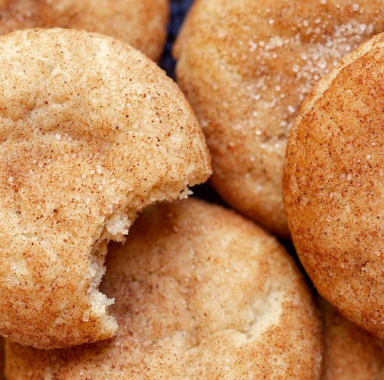 Close-up of golden snickerdoodle cookies coated in cinnamon sugar, with a bite taken out of one cookie.