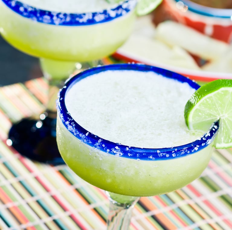 A classic lime margarita on ice in a salt-rimmed glass, garnished with a fresh lime wheel on a mat.