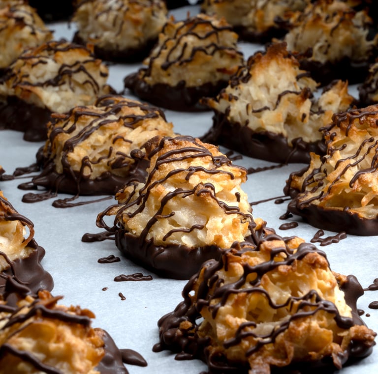 Golden, toasted coconut macaroon cookies drizzled with rich dark chocolate on a sheet of white parchment paper.