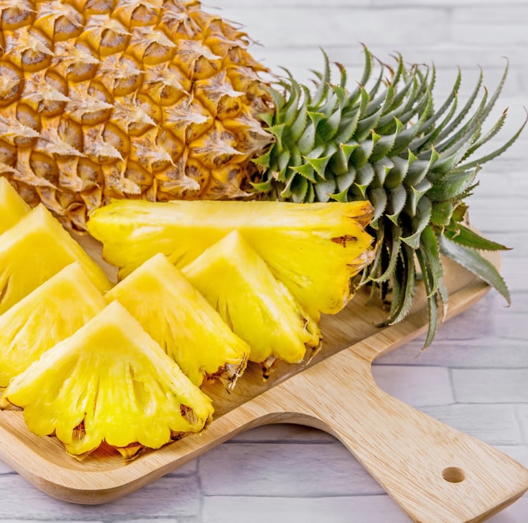 A whole fresh pineapple next to sweet, yellow sliced pineapple chunks on a wooden cutting board.