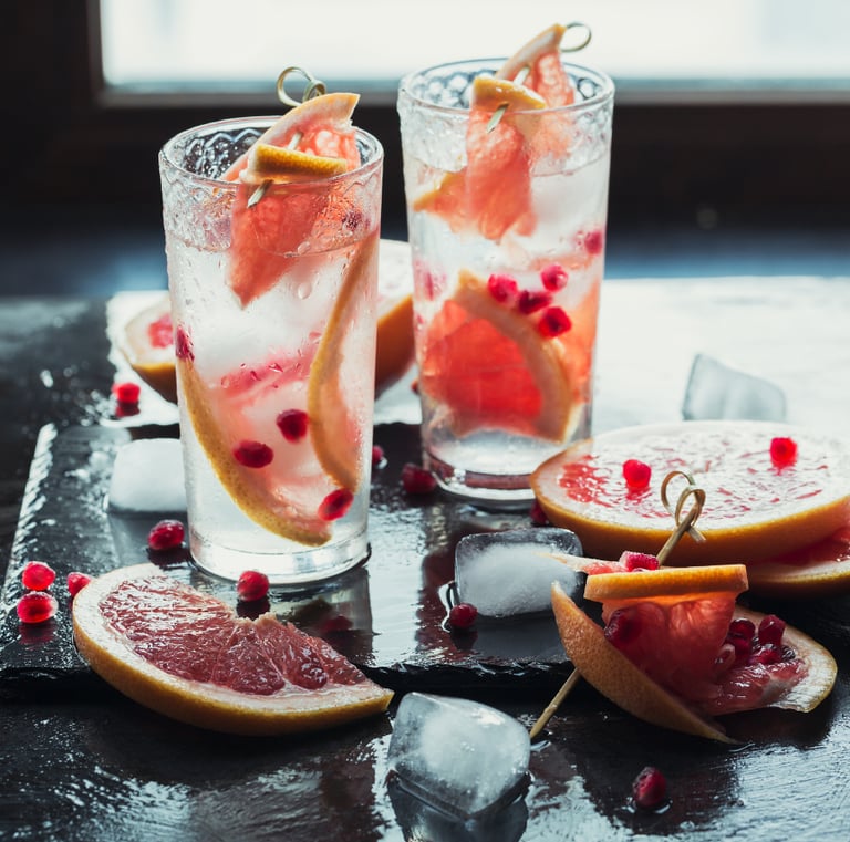 Two tall glasses of sparkling grapefruit drinks with ice, garnished with fresh grapefruit slices and pomegranate seeds.