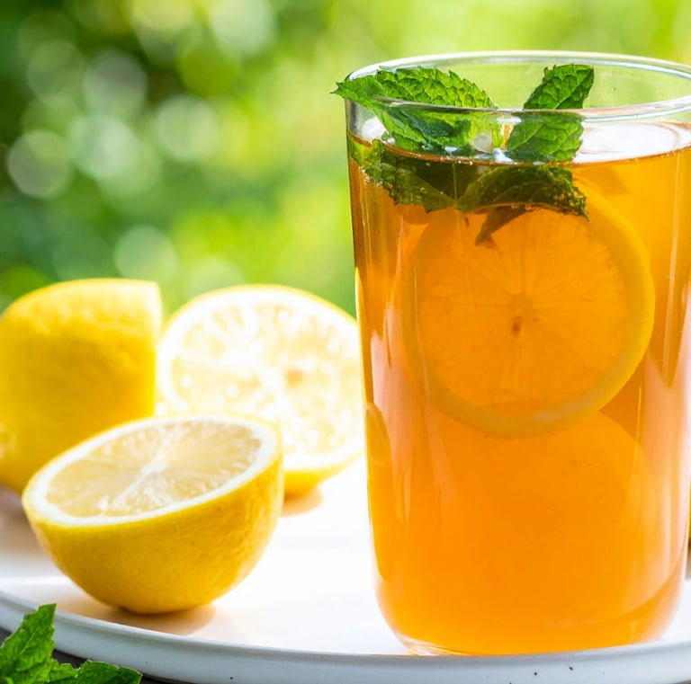 A tall, refreshing glass of iced sweet tea with sliced lemons and fresh mint leaves, shot on a sunny afternoon.