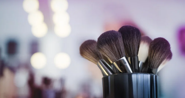 Makeup brushes in a black cup over a blurred, well-lit studio background