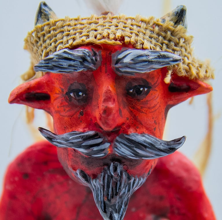 Red devil paper mask with horns, grey mustache, and a burlap headband.