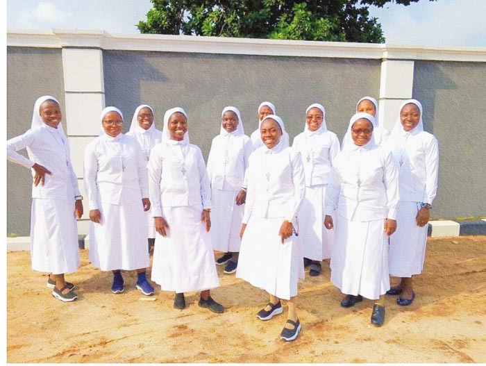 A group of smiling Catholic nuns in white habits posing together outdoors.