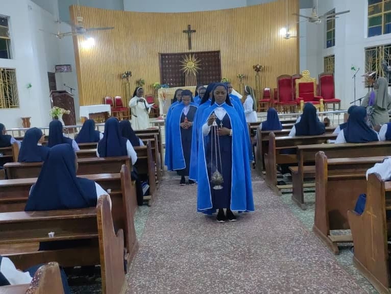 Catholic nuns in blue habits processing through a church aisle during a religious mass ceremony.
