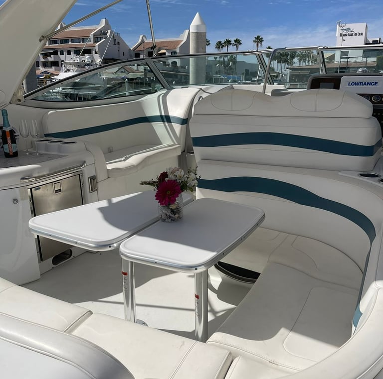 Luxury yacht deck with white leather seating, cockpit tables, and a champagne bottle near a sunny marina.