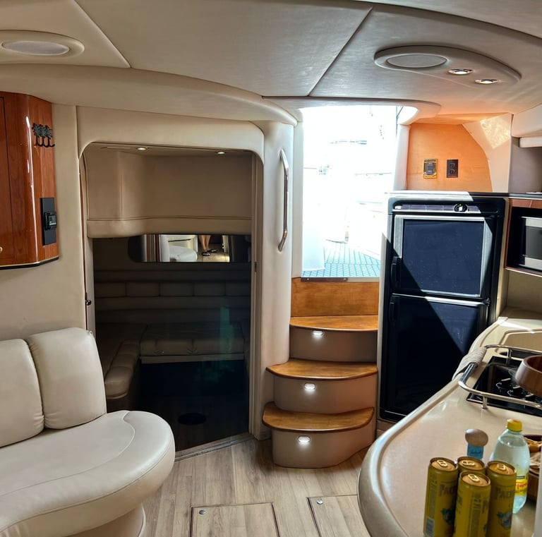 Luxury yacht cabin interior with leather seating, wooden cabinets, a compact galley kitchen, and stairs.