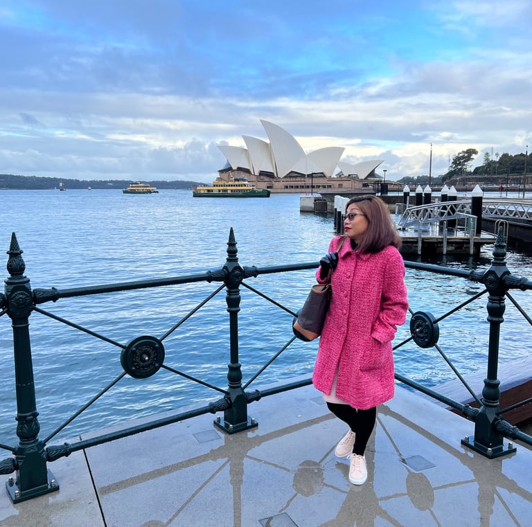 A woman in a pink coat stands on the foreground with the Sydney opera house in the background