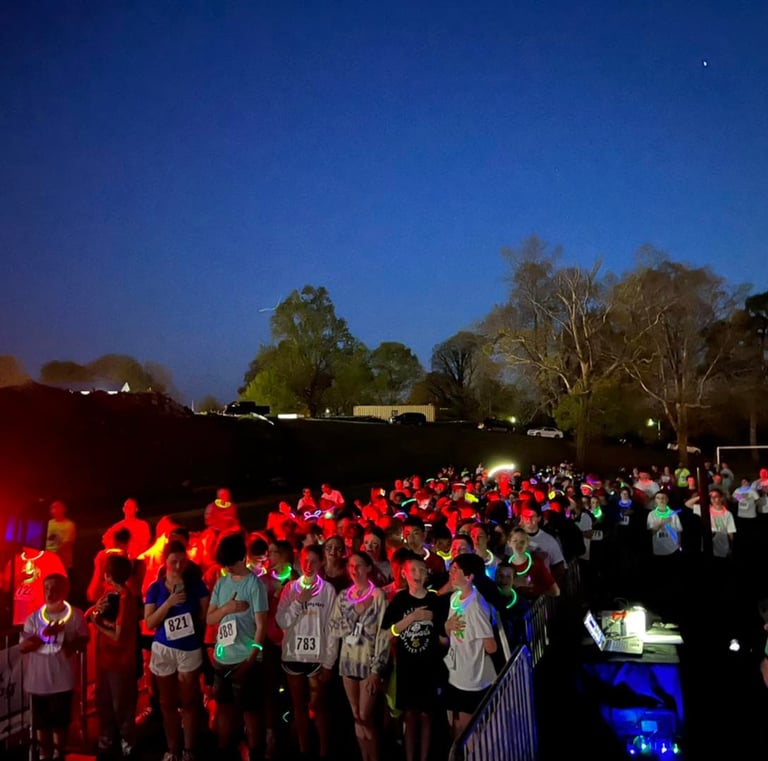 Racers lined up at the start line of a glow run event saying the pledge of allegiance