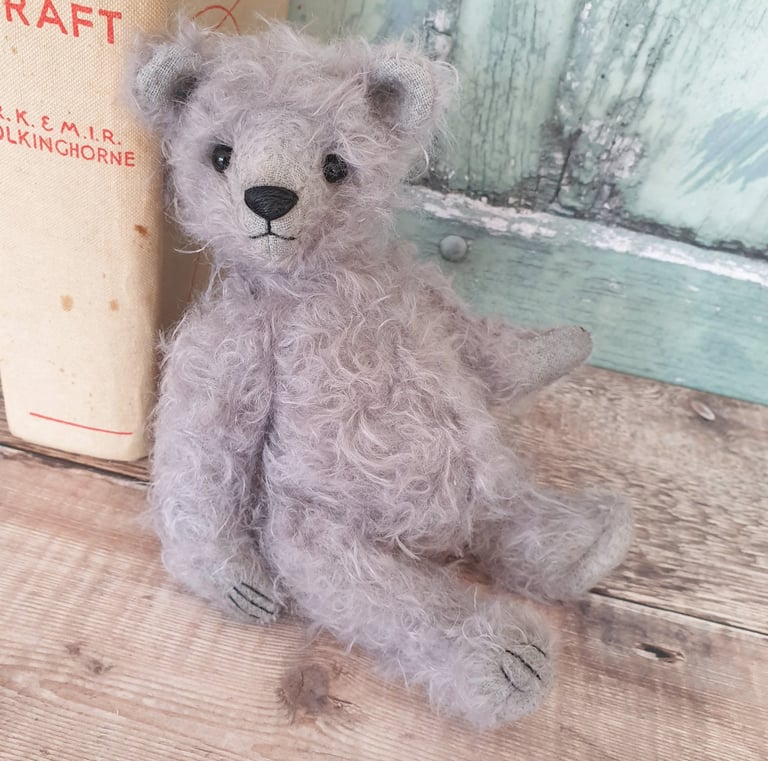 an adorable grey mohair handmade teddy bear leaning against a book