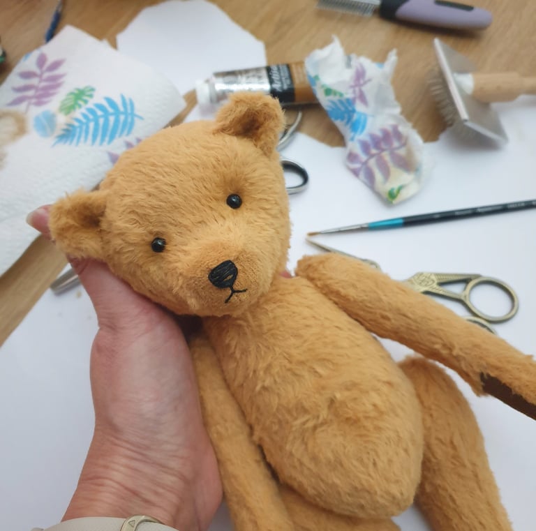 a teddy bear held in hands with art supplies in the background