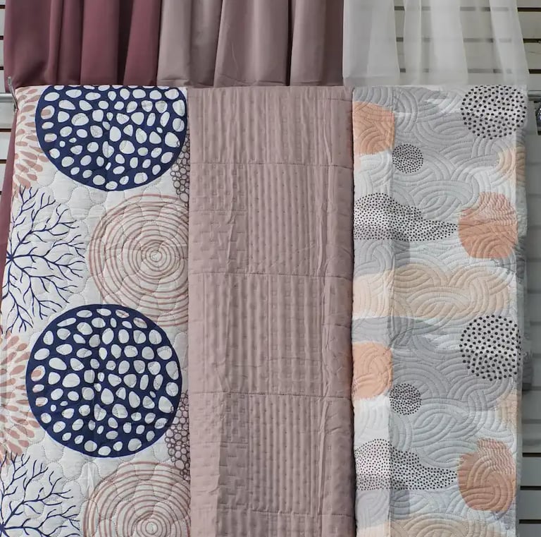 Muestras de colchas en frente de unas cortinas para enseñar los productos que se ofrecen.