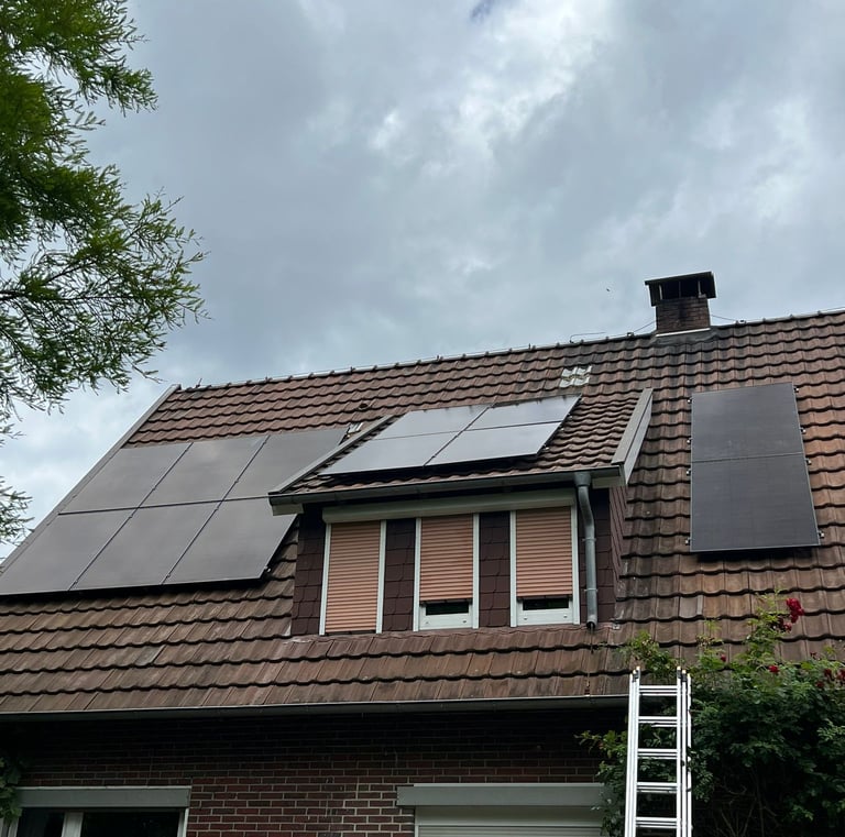 Black solar panels installed on a brown tile roof of a brick house under a cloudy sky.