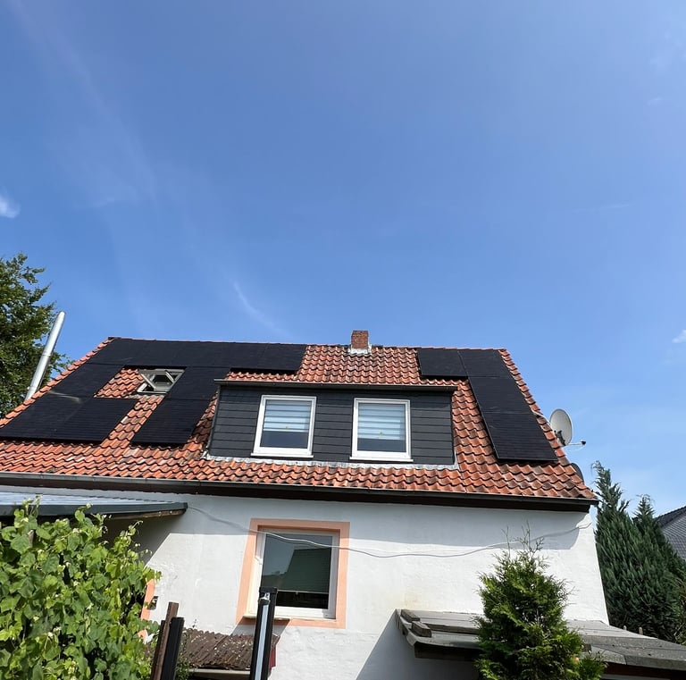 Residential house with black solar panels installed on a red clay tile roof under a clear blue sky.