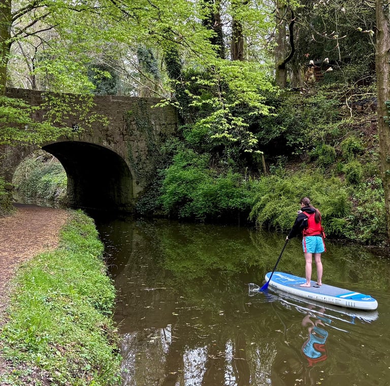 A paddle boarder paddles under a bridge on the Monmouthshire and Brecon canal on hire equipment from Bridge 76 Adventures