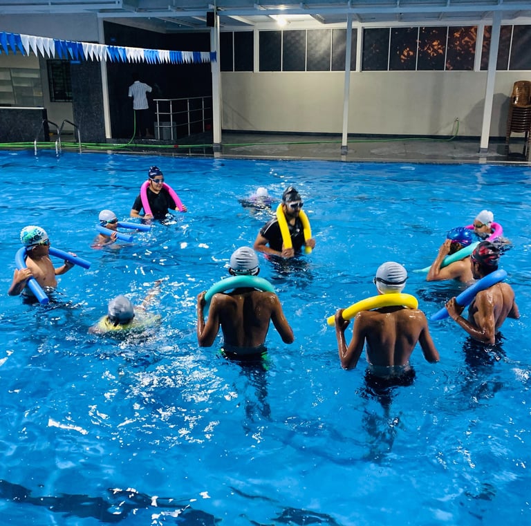 “Group of children in a swimming pool using floatation aids during a coached training session.”
