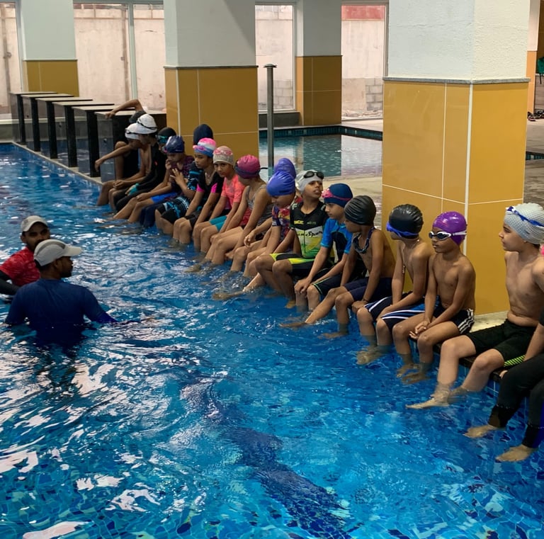 “Swimming coach instructing a group of kids seated at the pool edge.”