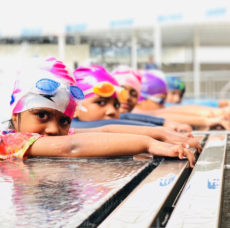 “Young swimmers in colorful caps resting on the pool edge during a lesson.”