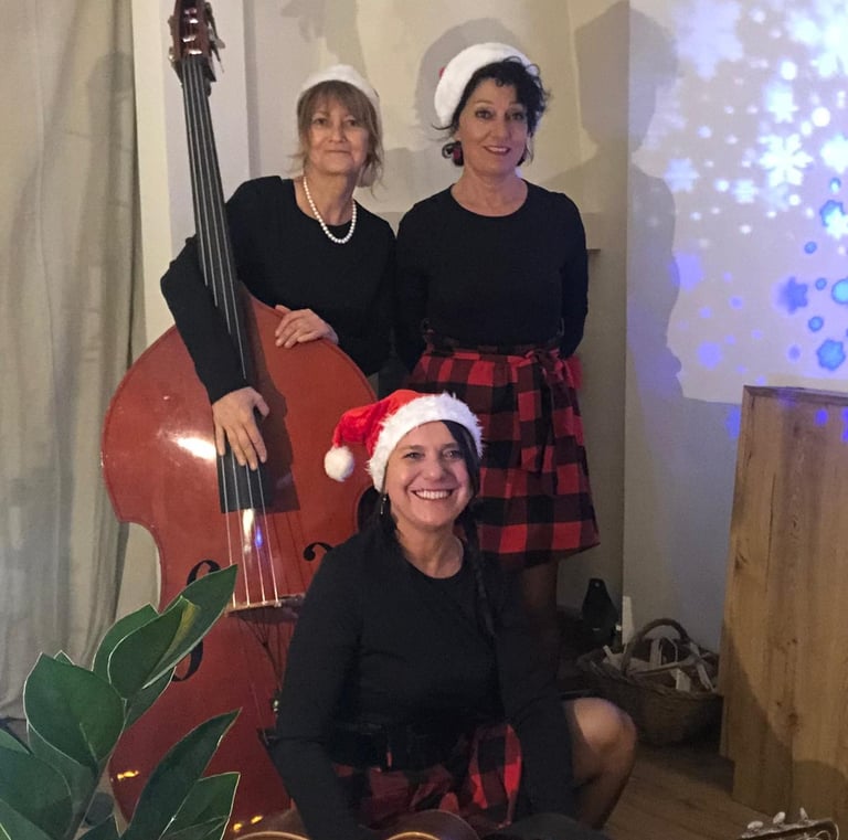 trois femmes en robe rouge et noire à carreaux avec des bonnets de Noël et une contrebassess