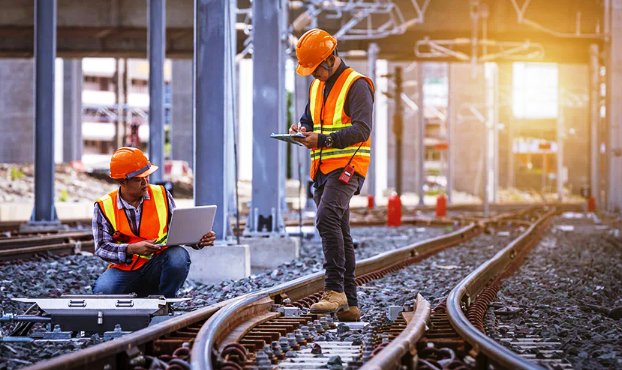 two men in safety vests standing on train tracks