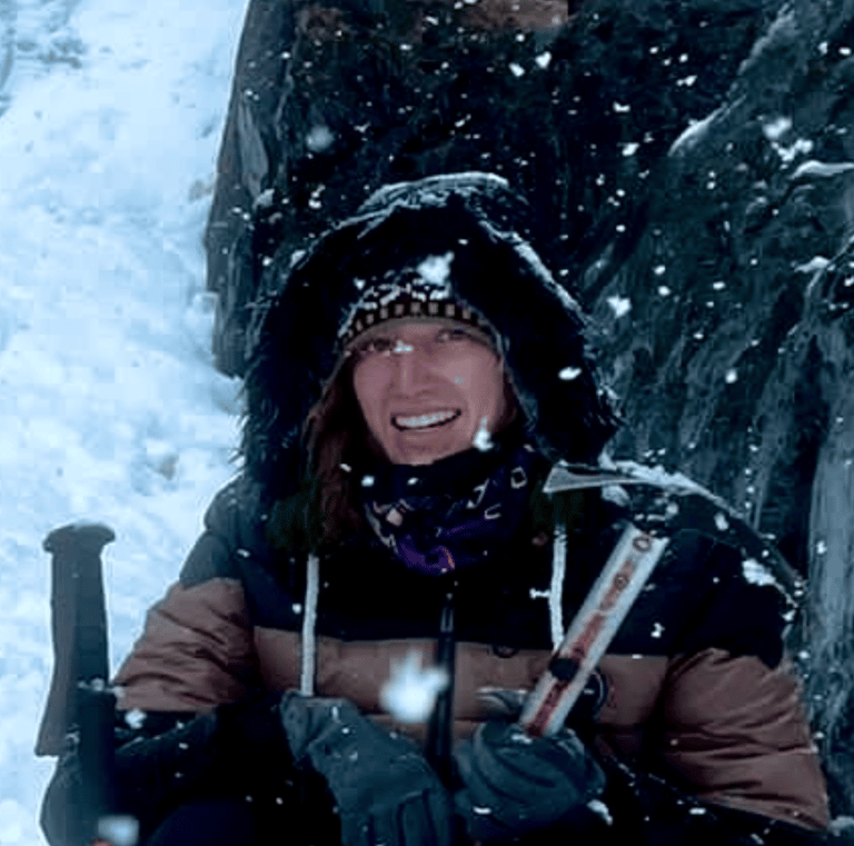 Smiling woman holding an ice axe while winter hiking and mountain climbing in the snow.