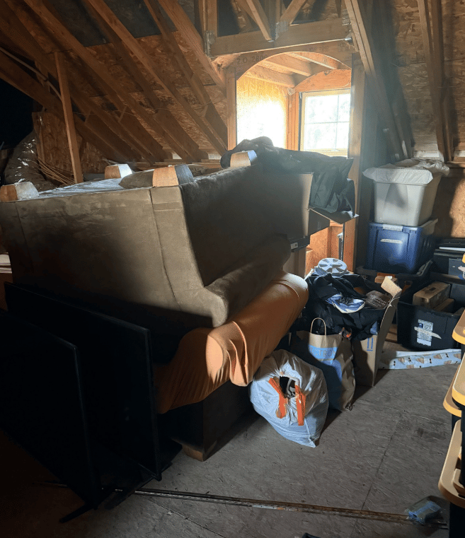 An attic full of junk including a couch and chair and a bunch of trash bags