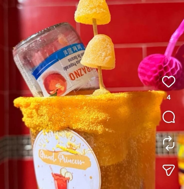 Mexican michelada drink with chili powder rim, peach candy skewers, and an inverted juice bottle.