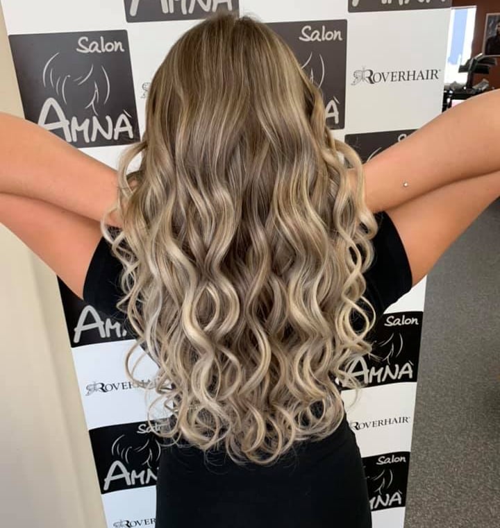 Woman with long blonde balayage hair styled in loose curls at Salon Amna.