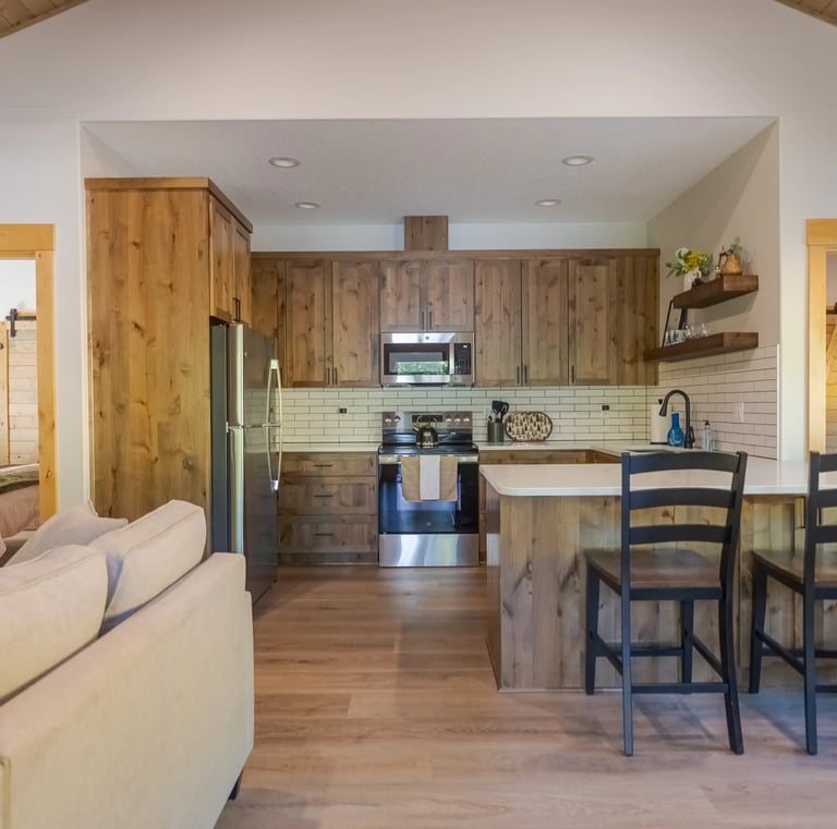 Modern rustic kitchen with wood cabinets, stainless steel appliances, and a breakfast bar with black stools.