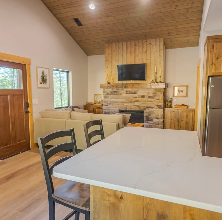 Rustic modern cabin interior with stone fireplace, wood vaulted ceiling, and white kitchen island.