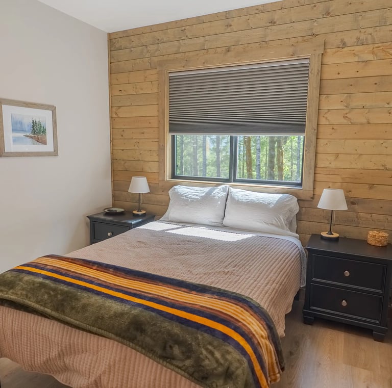 Cozy rustic bedroom with a wooden accent wall, queen bed, and forest views through the window.