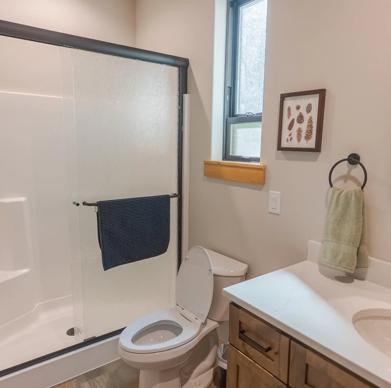 Modern bathroom interior featuring a walk-in shower with sliding glass doors, white vanity, and rustic wall decor.