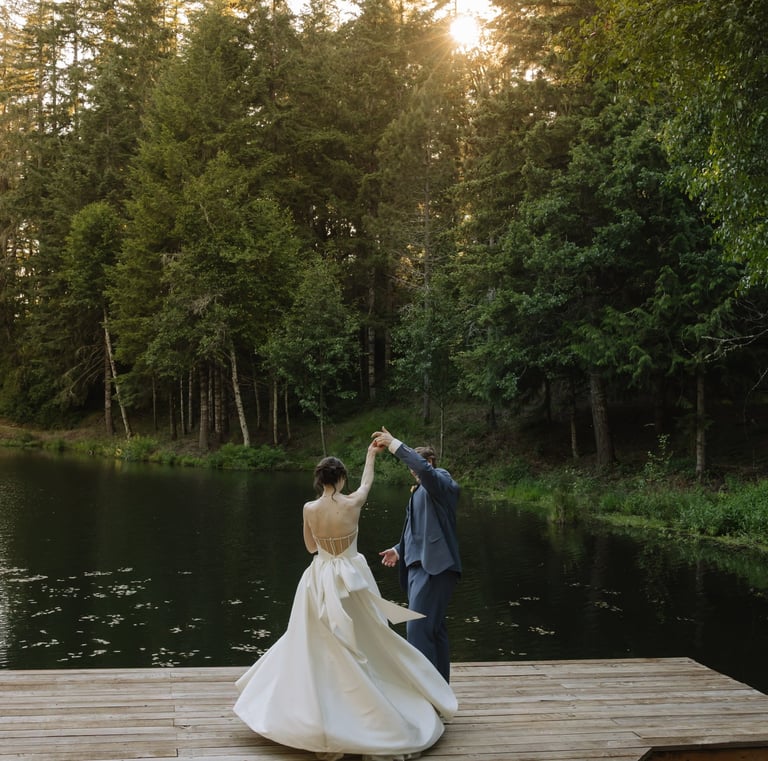 A bride and groom dancing on a wooden dock by a serene lake during an outdoor forest wedding.