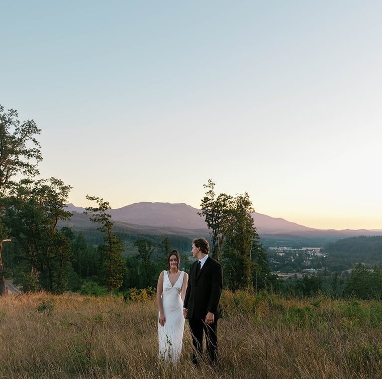 A bride and groom standing in a grassy field during a mountain sunset wedding.