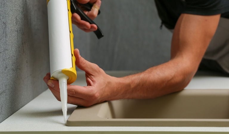 Plumber applying silicone sealant around kitchen sink installation