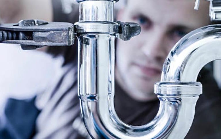 Plumber repairing pipe connection with wrench under sink