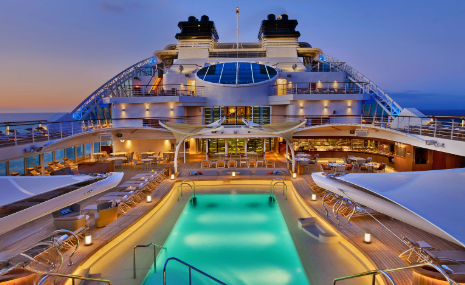 Carnival cruise ship pool deck at sunset with illuminated swimming pool and lounge areas.