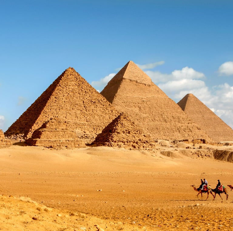 Great Pyramids of Giza in Egypt with tourists riding camels across the desert sand.