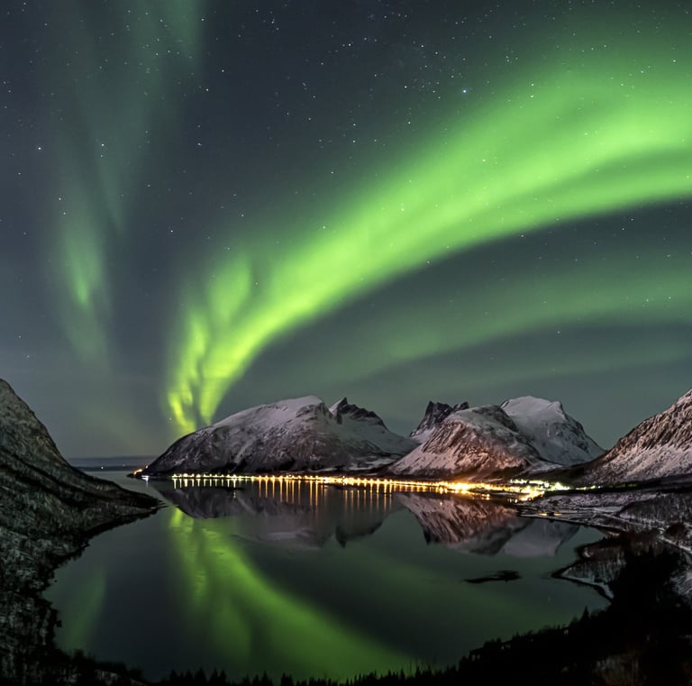 Vibrant green aurora borealis dancing over snow-capped mountains and a fjord in Norway.