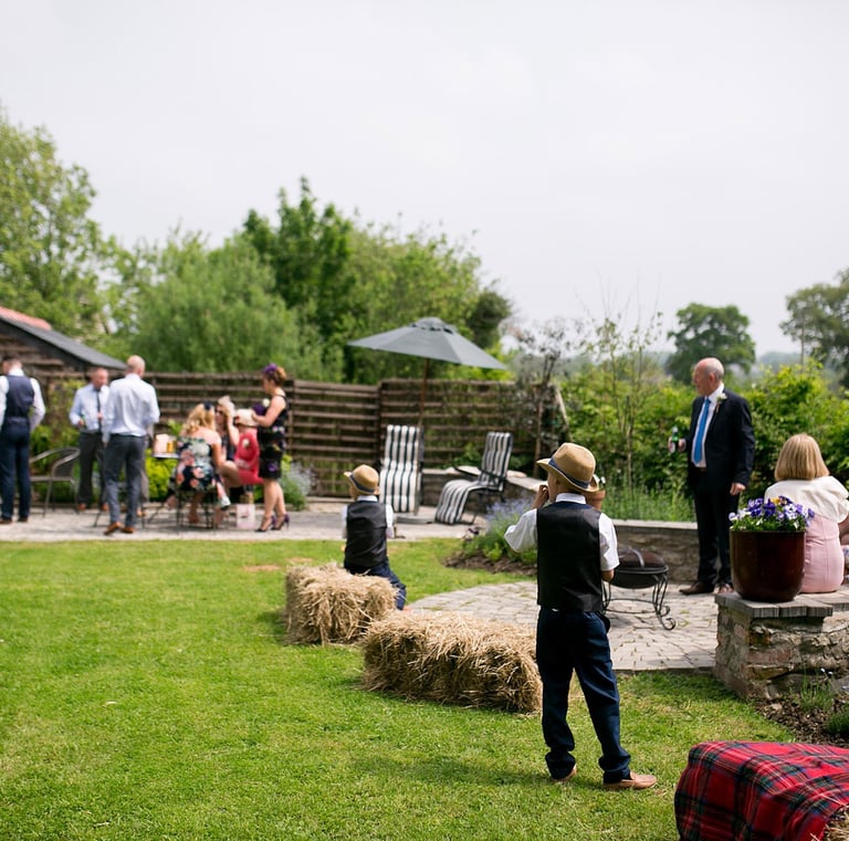 Guests enjoying an outdoor wedding reception on a sunny patio with hay bale seating.